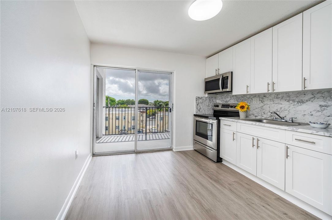 Kitchen featuring white cabinetry, stainless steel appliances, patterned stone-look backsplash, wood-finish flooring, and sliding glass doors leading to a private balcony