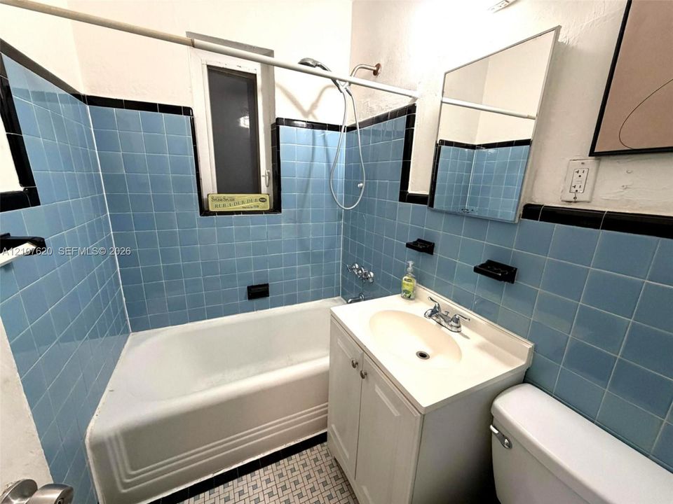 Bathroom featuring blue square wall tiles with black trim, porcelain tub with shower head, vanity cabinet with integrated sink, and mosaic tile flooring