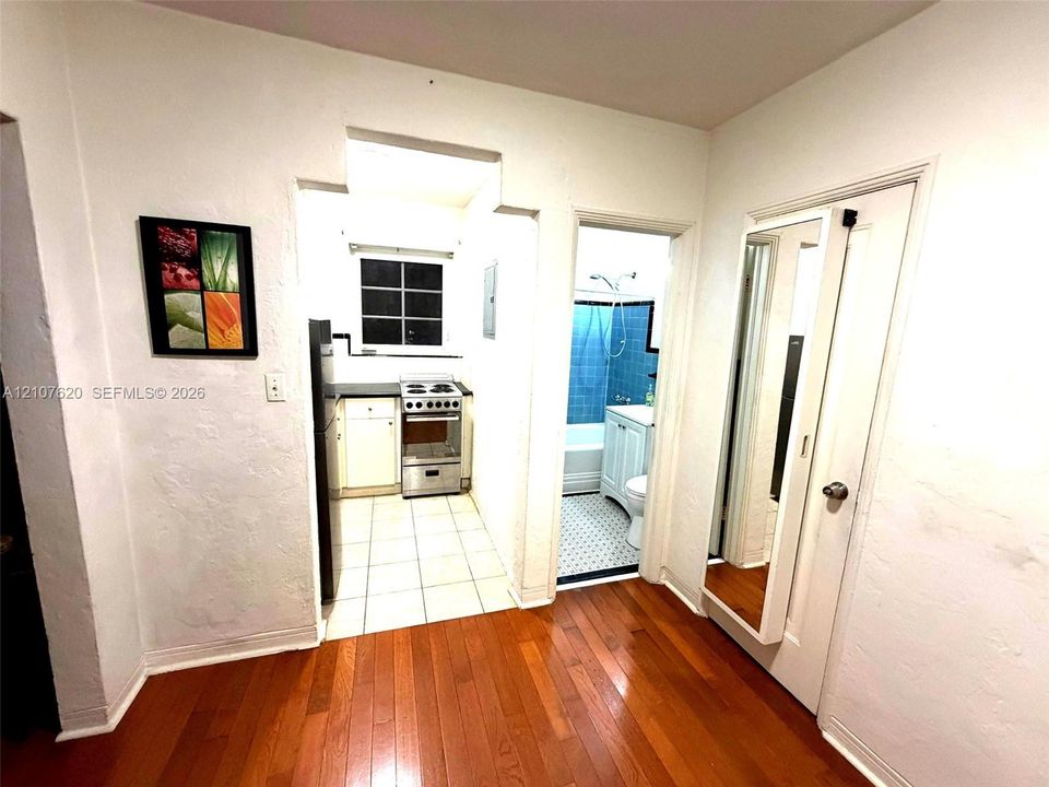 Wood-finish flooring, kitchen featuring a stainless steel range and ceramic tile flooring, bathroom with patterned tile flooring and blue wall tiling, and a door featuring an integrated full-length mirror