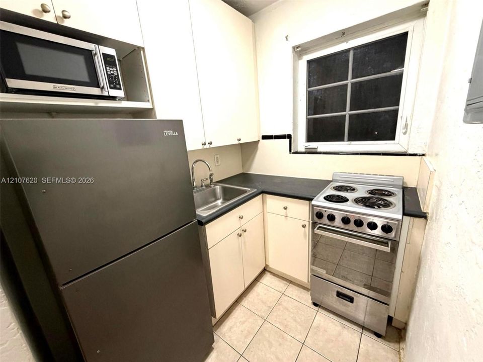Kitchen featuring white flat-panel cabinetry, dark countertops, a stainless steel sink with a curved faucet, a stainless steel range, and tile flooring