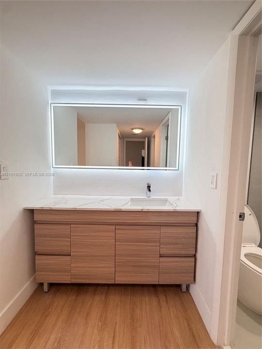 Wood-finish vanity with four drawers and dual cabinet doors, quartz countertop with integrated sink, chrome faucet, and rectangular LED-backlit mirror