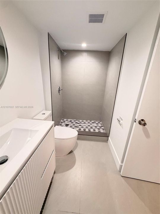 Bathroom featuring a white fluted-front vanity with an integrated sink, floor-to-ceiling large-format wall tiling, and a shower floor finished with hexagonal mosaic tiles