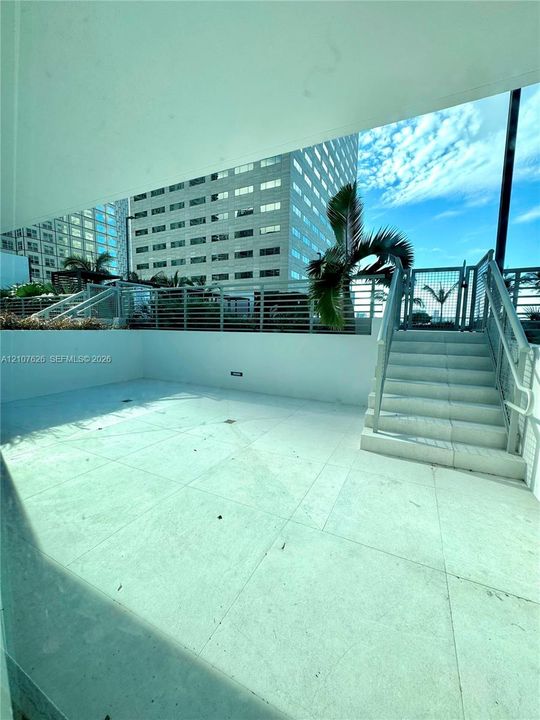 Outdoor terrace featuring large-format tile flooring, a metal staircase with matching handrails, and perimeter metal fencing