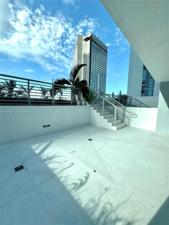 Outdoor terrace featuring large-format tile flooring, metal stair railings, and integrated perimeter lighting