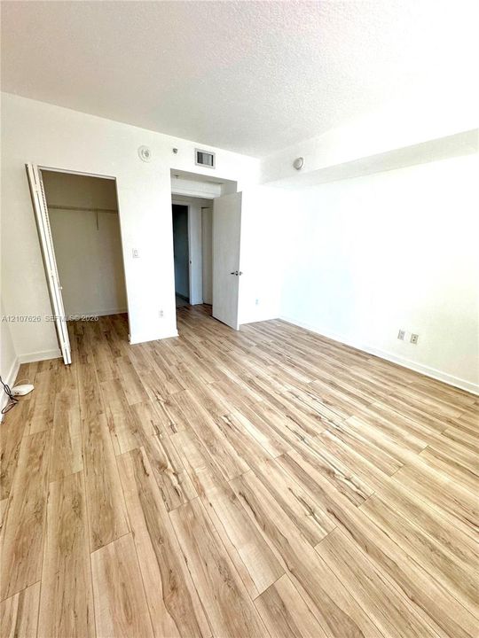 Room featuring wood-finish flooring, white walls, and a closet with a built-in rod