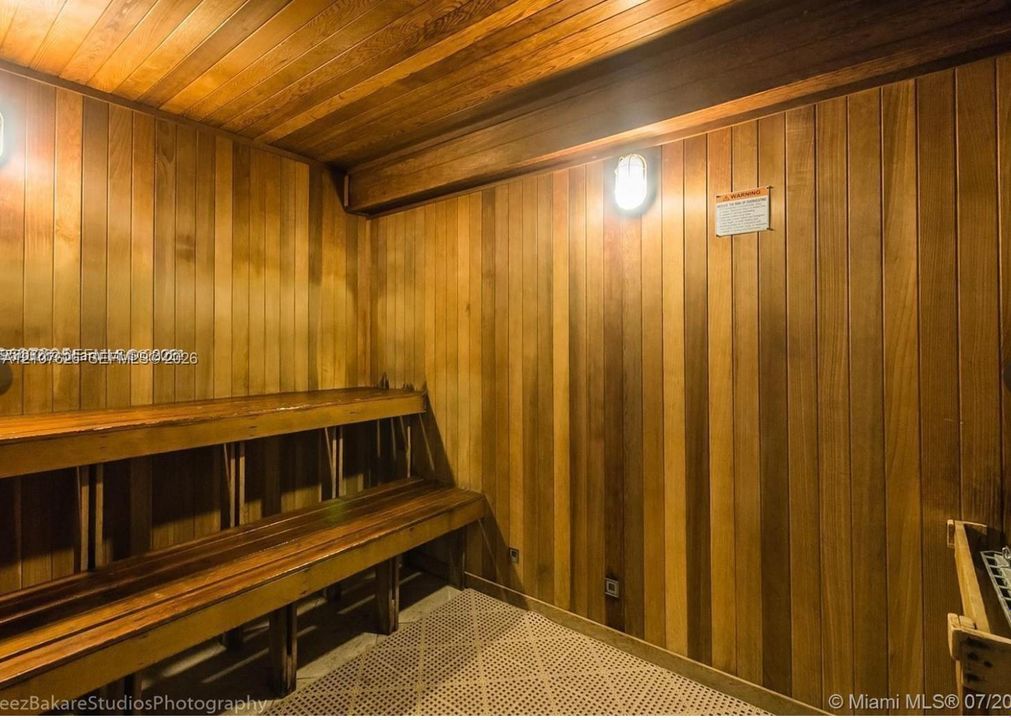 Sauna room featuring full wood-paneled walls, tongue-and-groove ceiling, multi-level built-in bench seating, and wall-mounted bulkhead lighting
