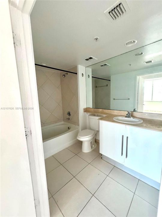 Bright, well-appointed bathroom featuring ceramic tile flooring, a white vanity with dual-sink configuration and wood-finish countertop, recessed ceiling lighting, and an alcove bathtub with tile surround and integrated shower enclosure