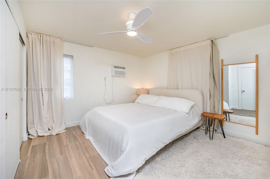 Interior room featuring wood-finish flooring, a contemporary three-blade ceiling fan, and a wall-mounted climate control unit