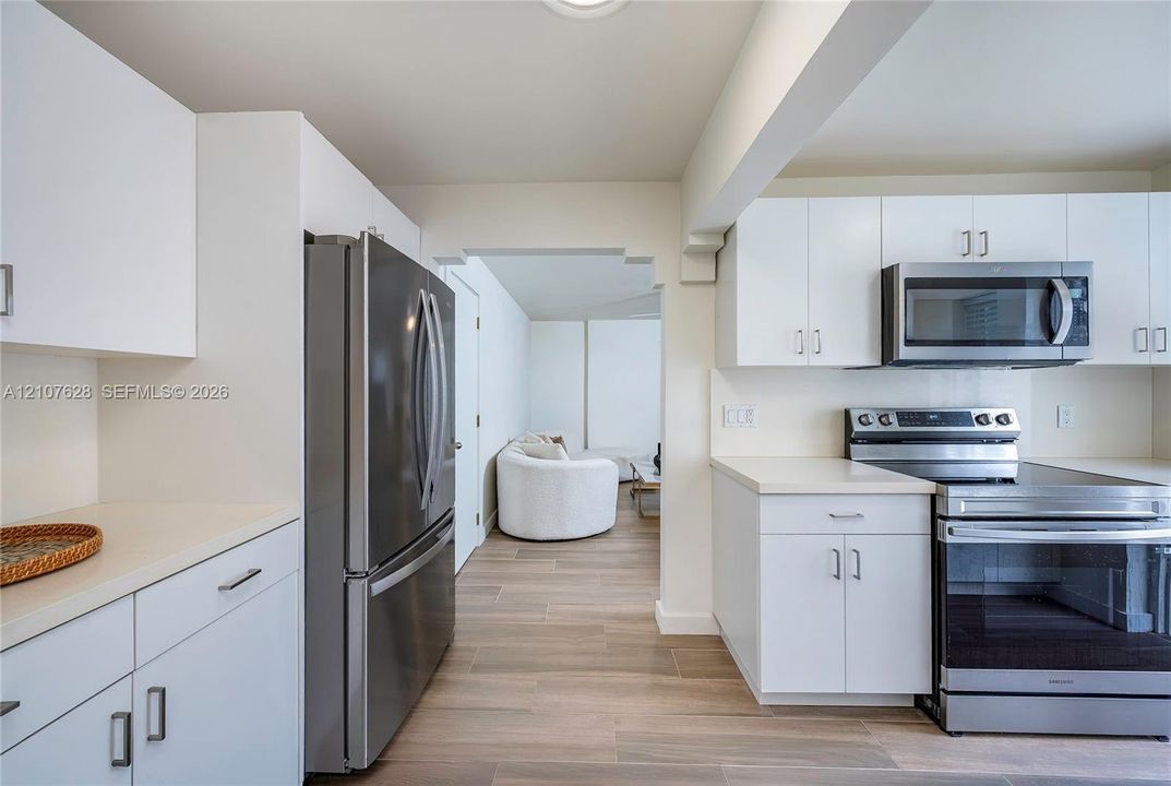 Kitchen featuring white cabinetry, stainless steel appliances, wood-finish flooring, and solid-surface countertops