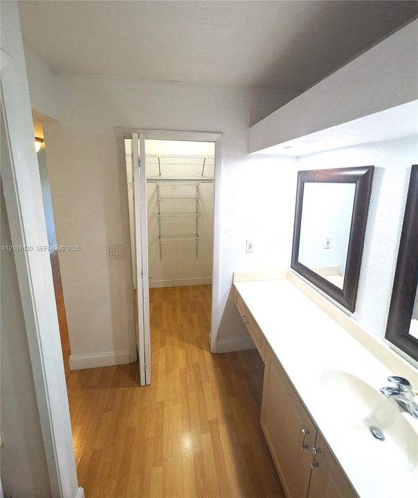 Vanity featuring a light wood finish cabinet, integrated countertop, and mounted mirrors, including a closet with wire shelving and wood-finish flooring