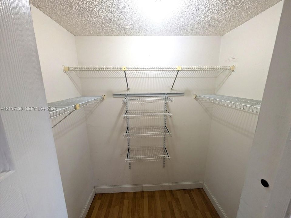 Walk-in closet featuring white wire shelving, a multi-tier hanging organizer, and wood-finish flooring