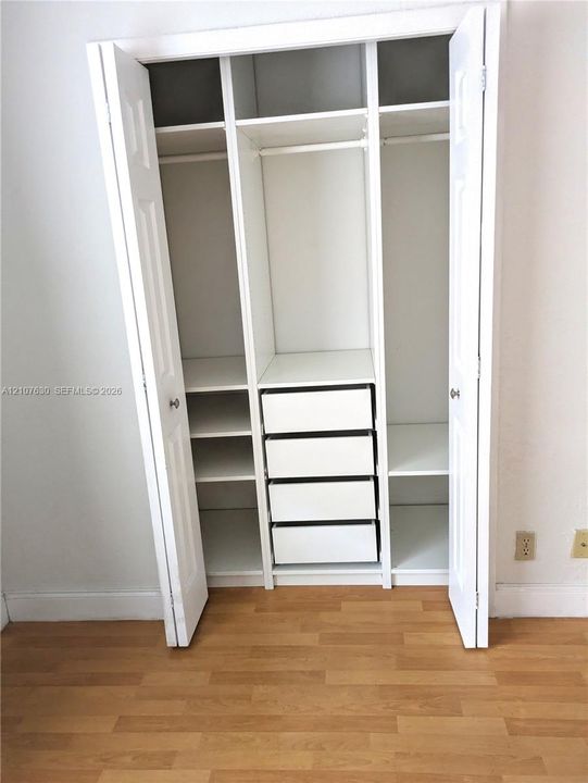 Built-in closet featuring white cabinetry, multiple overhead storage shelves, integrated hanging rods, and four pull-out drawers