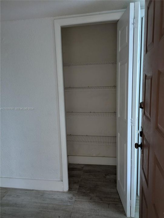 Storage closet featuring multi-tier wire shelving and white paneled door, set against wood-finish flooring