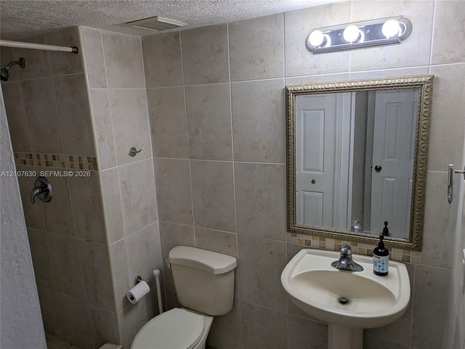 Bathroom featuring beige wall tiles with a glass mosaic accent band, a white pedestal sink with a chrome faucet, a framed wall mirror, and a walk-in shower