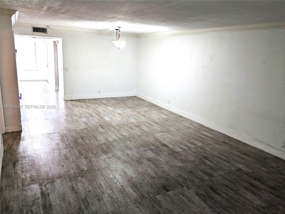 Wood-finish flooring, neutral wall tones, crown molding, and a central pendant light fixture
