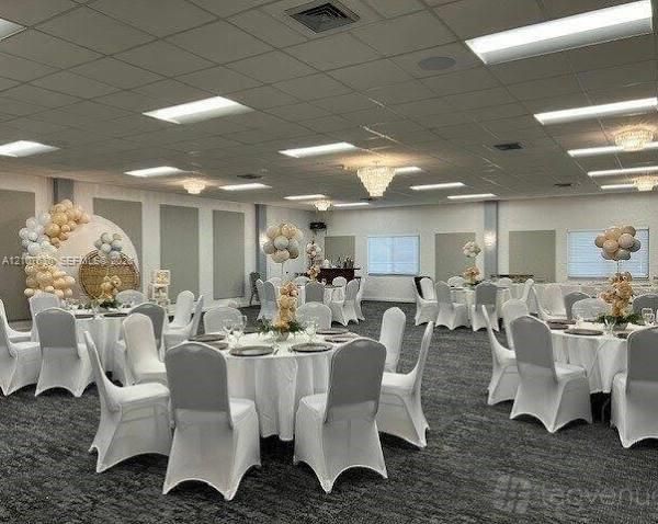 Expansive event hall featuring a drop ceiling with integrated recessed lighting, multiple crystal-style chandeliers, neutral-toned wall panels, and wall-to-wall carpeting