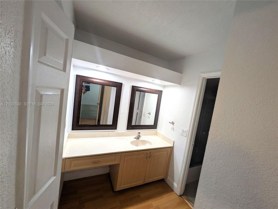 Bathroom vanity featuring light wood-finish cabinetry, an integrated sink basin, dual wall-mounted mirrors with dark frames, and recessed lighting