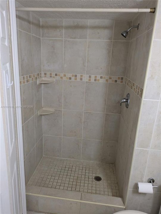 Walk-in shower featuring neutral tile surround, integrated corner shelving, mosaic tile accent inlay, and metal shower hardware