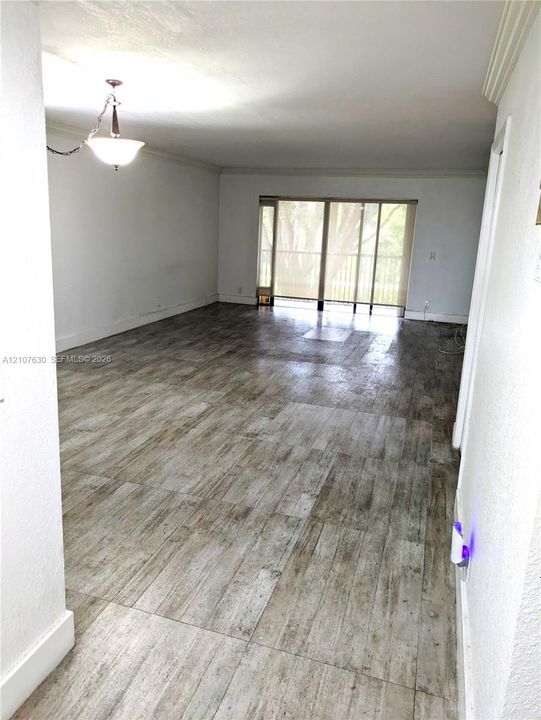 Open-concept interior featuring wood-finish tile flooring, a multi-light pendant fixture, and sliding glass doors with balcony access