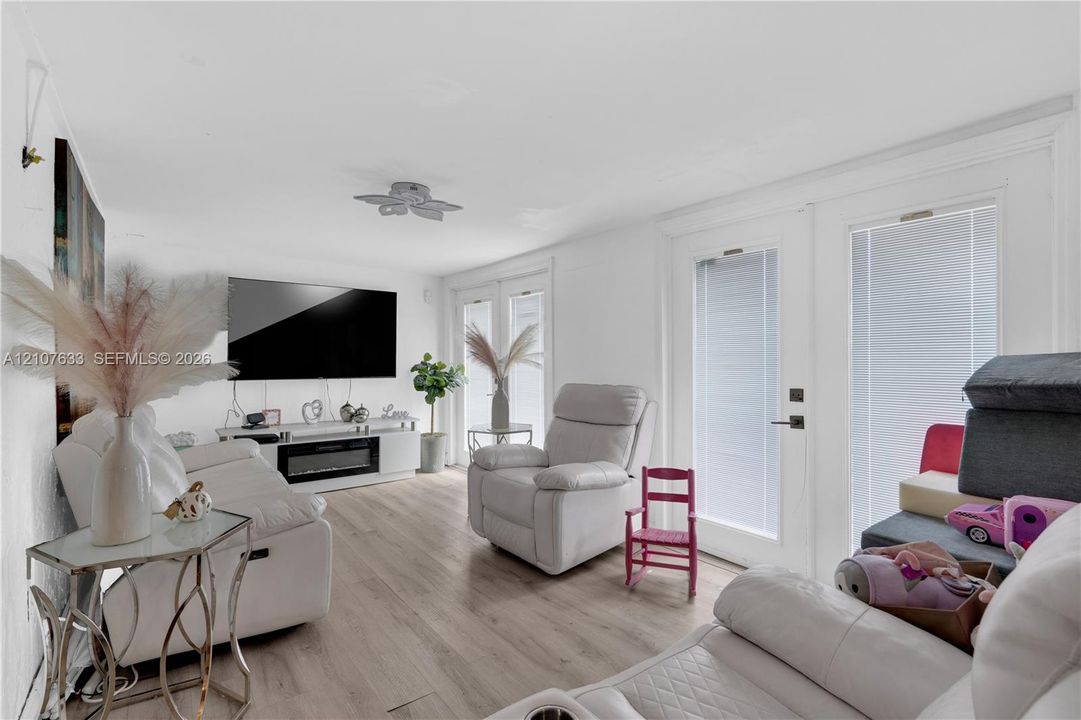 Living area featuring light-toned wood-finish flooring, recessed lighting, and dual glass-paned doors with integrated blinds