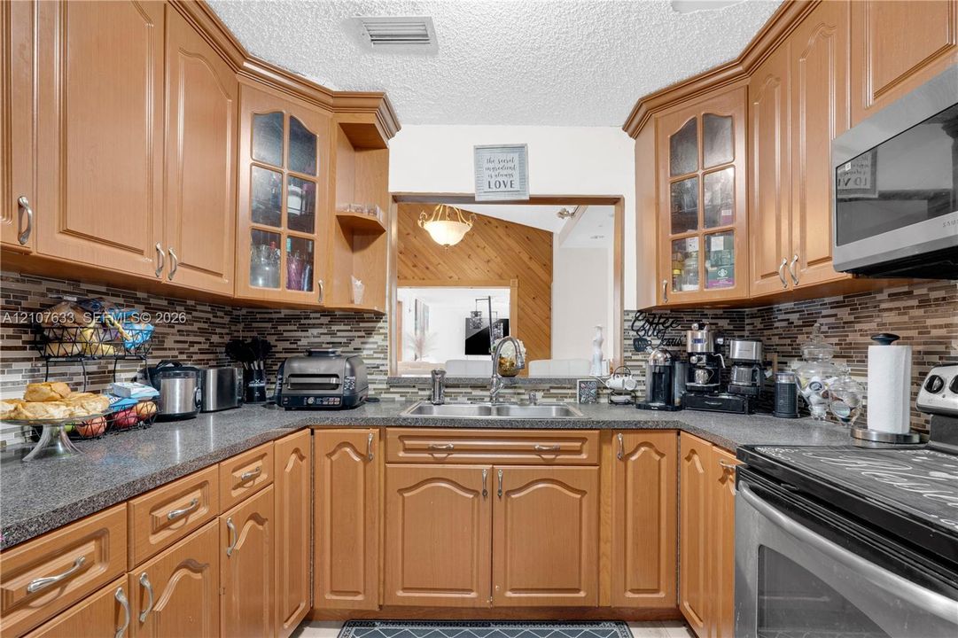 Kitchen featuring stained wood cabinetry with glass-front uppers, stone-pattern backsplash, stainless steel appliances, and a double-basin sink