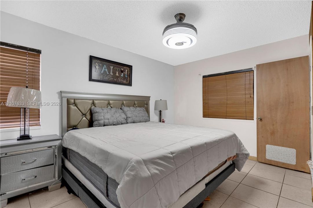 Neutral-toned interior space featuring light-colored ceramic tile flooring, horizontal slatted window blinds, and a circular drum-style ceiling light fixture