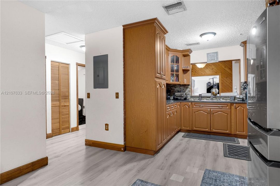 Kitchen featuring wood cabinetry, integrated glass-front display storage, multi-toned tile backsplash, and light-toned wood-finish flooring