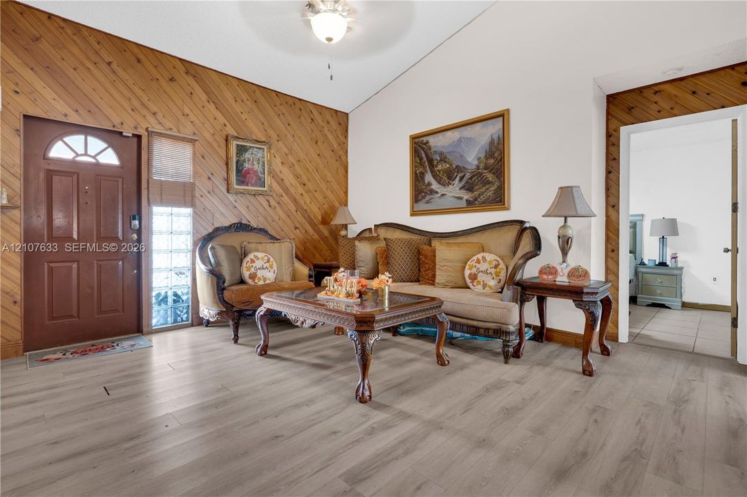 Interior space featuring diagonal wood-plank wall paneling, vaulted ceiling, wood-finish flooring, glass block accent window, and an arched-top front door