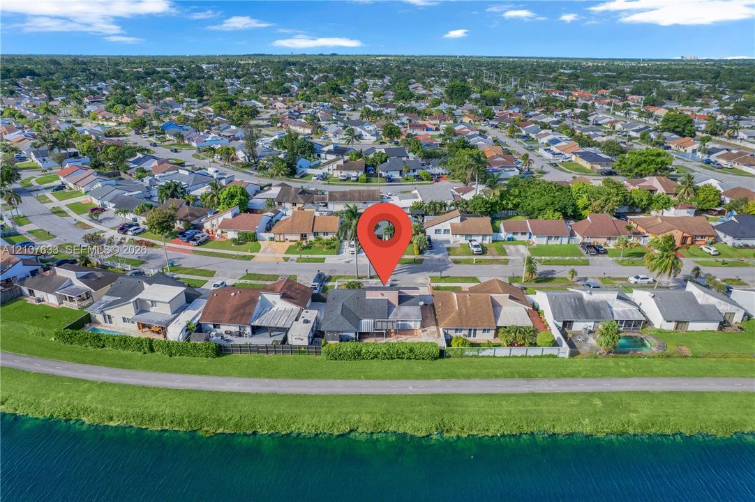 Aerial perspective featuring a waterfront property with a concrete patio, perimeter shrubbery, and shingle roofing