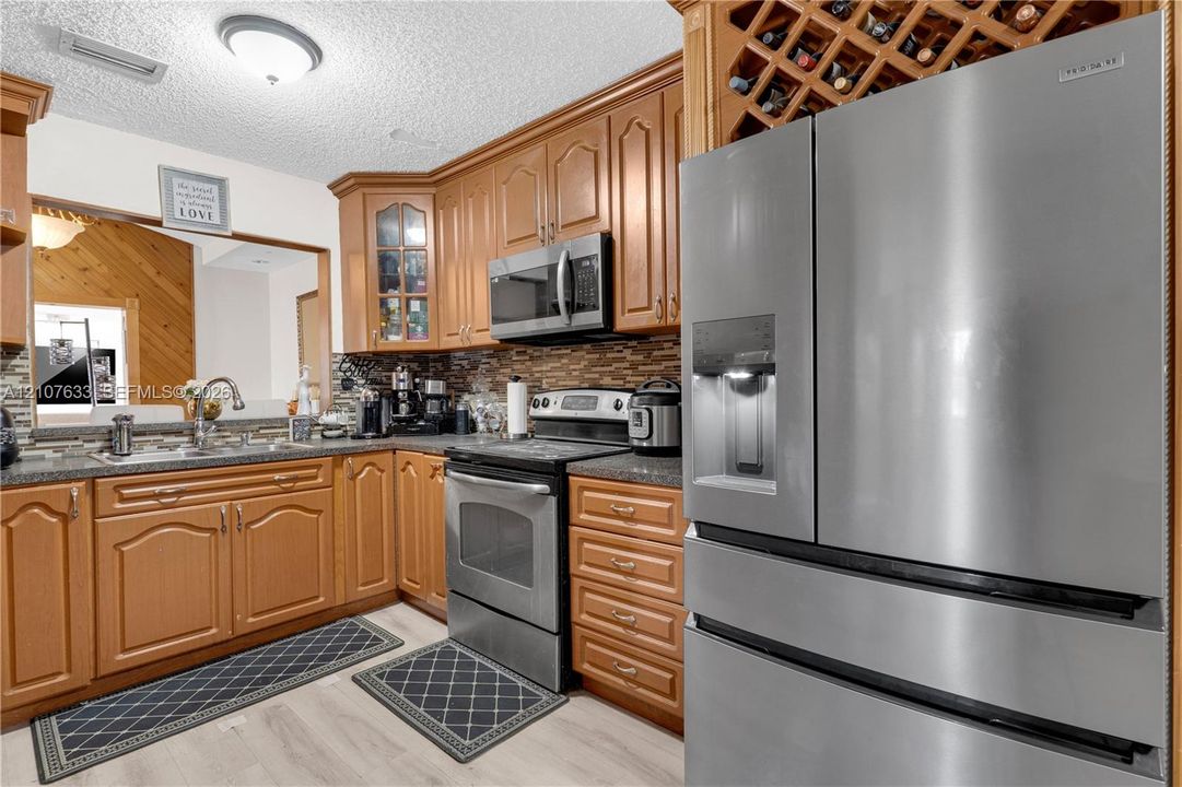 Kitchen featuring natural wood cabinetry, built-in wine storage, stainless steel appliances, stone-look countertop, and a decorative tile backsplash
