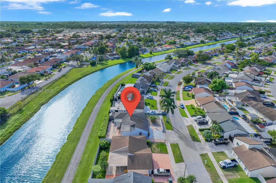 Aerial perspective of a single-family residence featuring a concrete tile roof, attached garage, paved driveway, and direct canal frontage