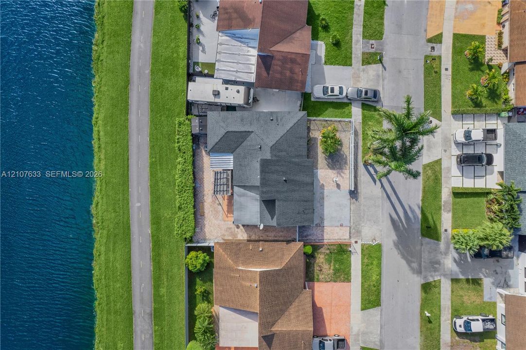 Aerial perspective of waterfront property featuring a paved rear patio, pergola, and direct access to a paved perimeter path