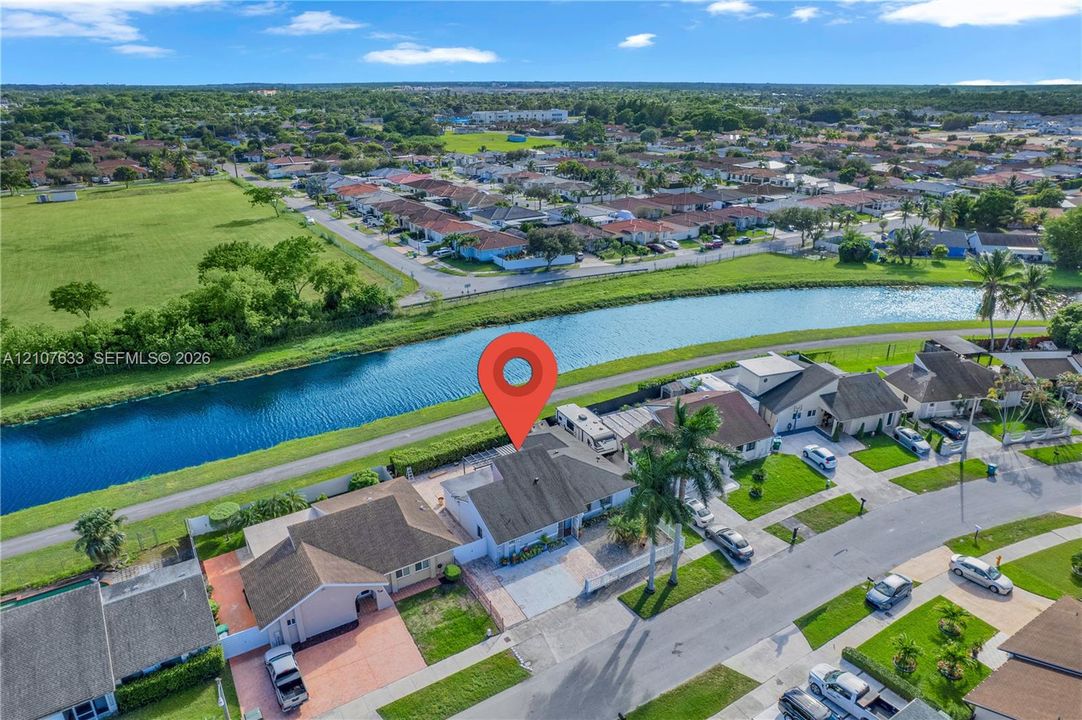 Aerial perspective featuring a single-story residence with a concrete tile roof, paved driveway, and a backyard area bordering a canal