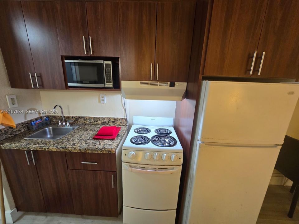 Kitchenette featuring dark wood-finish cabinetry, stone-patterned countertops, stainless steel sink with high-arch faucet, built-in microwave, and electric range