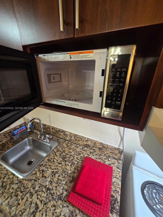 Built-in microwave with stainless steel finish, stone-surface countertop, and stainless steel drop-in sink with gooseneck faucet