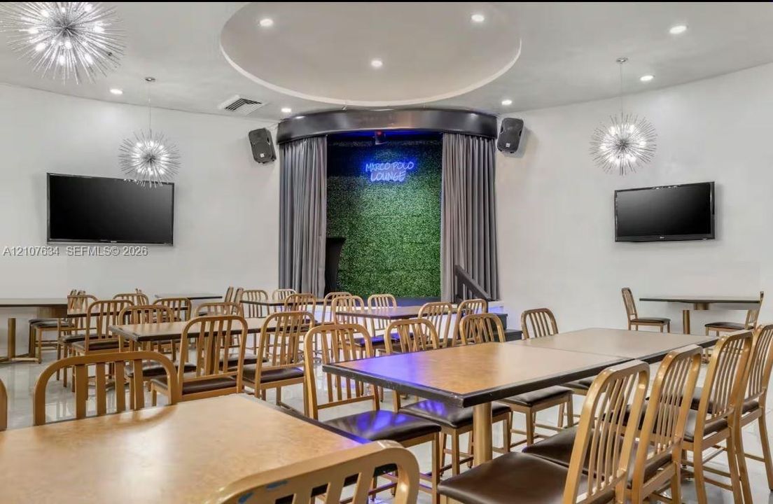 Entertainment space featuring a recessed stage with curtain backdrop, built-in sound system, decorative starburst pendant lighting, and a circular tray ceiling