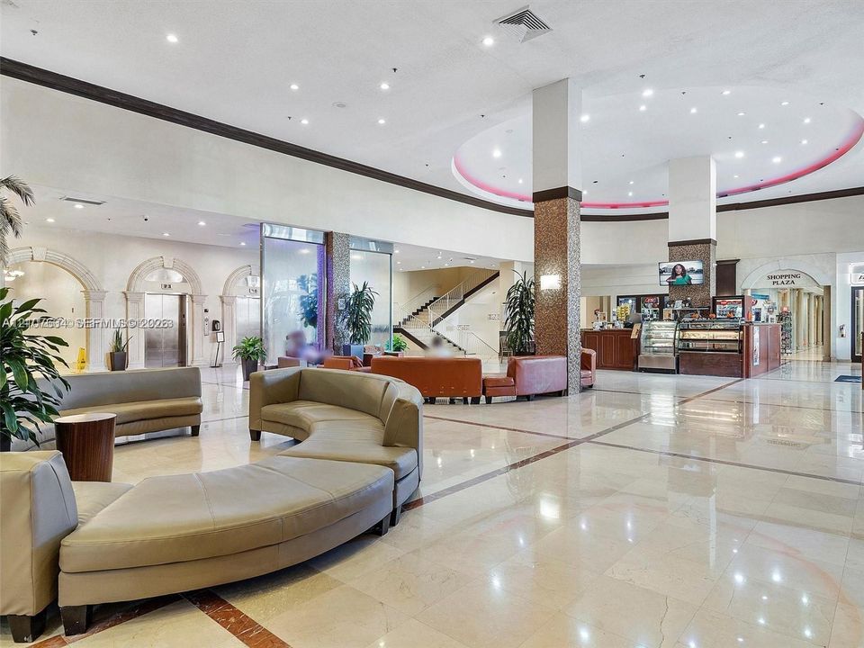 Expansive lobby featuring polished stone flooring with decorative inlays, recessed ceiling lighting, textured stone-finish columns, and arched architectural entryways