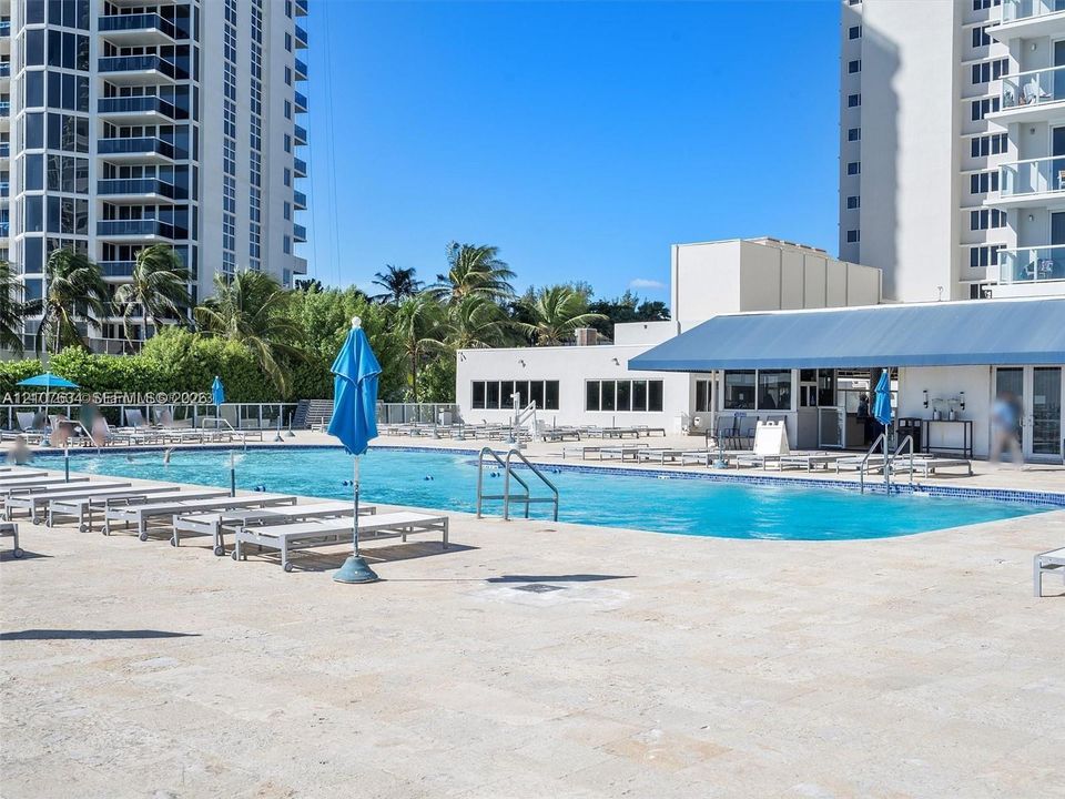 Resort-style swimming pool featuring a tiled finish, expansive stone-paved deck, and a shaded outdoor pavilion