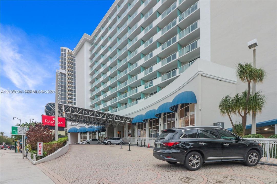 High-rise exterior featuring stacked cantilevered balconies, decorative blue fabric awnings, a paved circular drive, and multi-story glass-paned ground level frontage