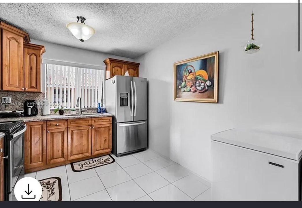 Kitchen featuring warm-toned wood cabinetry, stone countertops, stainless steel appliances, and white tile flooring