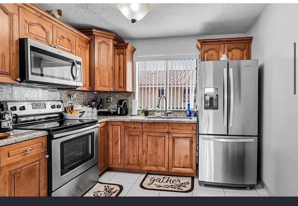 Kitchen featuring wood cabinetry, stone countertops, stainless steel appliances, tiled flooring, and a sink with a gooseneck faucet