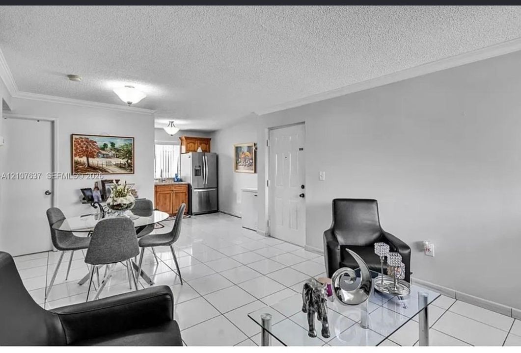 Open-concept living space featuring large-format ceramic tile flooring, neutral wall tones, recessed ceiling lighting, and crown molding