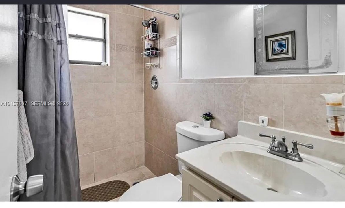 Bathroom featuring floor-to-ceiling neutral wall tile, integrated vanity with a molded sink, dual-handle metal faucet, and wall-mounted vanity mirror