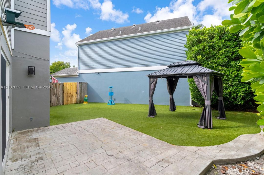 Fenced backyard featuring synthetic turf, paver patio, and metal gazebo