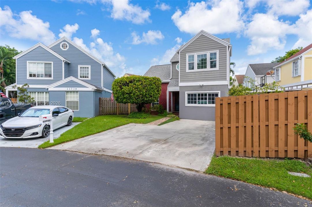 Two-story exterior featuring grey horizontal siding, multi-pane windows, a concrete driveway, and a wood-slat privacy fence