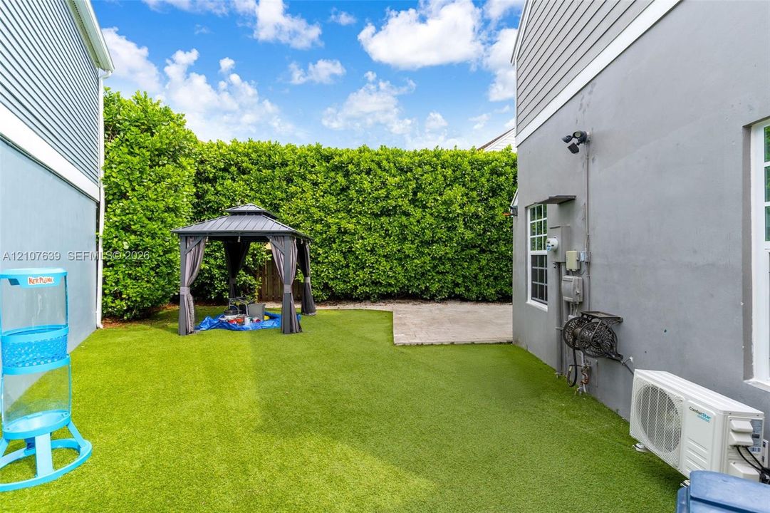 Private backyard featuring artificial turf, a paved patio area, and dense perimeter hedging