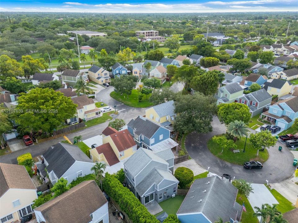 Aerial perspective of a residential neighborhood featuring paved streets, mature trees, manicured landscaping, and detached single-family dwellings with diverse rooflines
