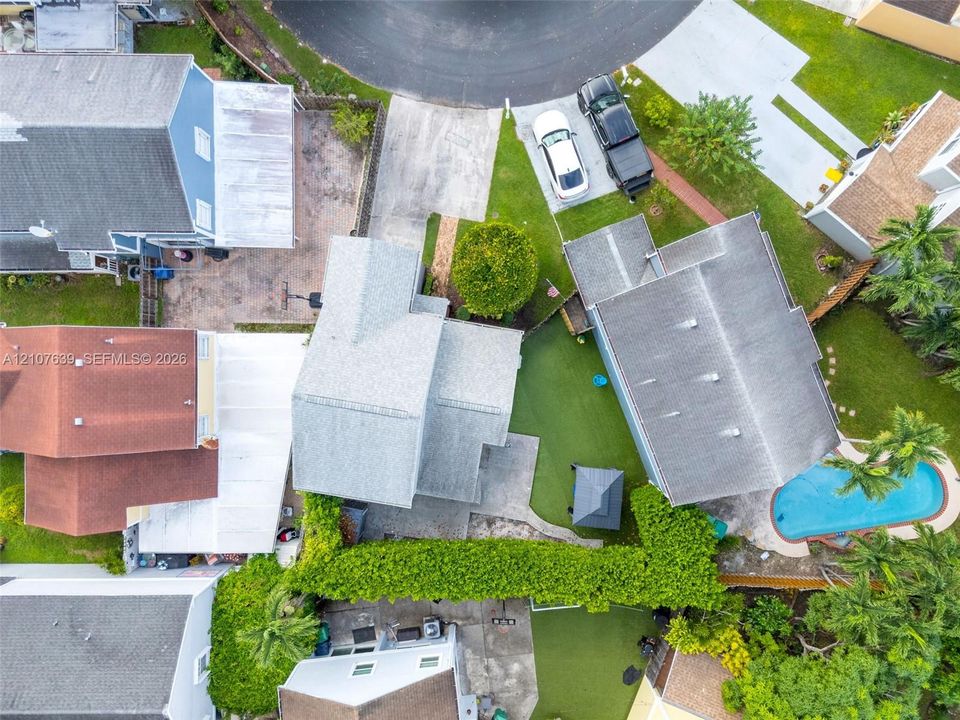 Aerial perspective of property featuring a private swimming pool, concrete patio, artificial turf lawn, and mature perimeter landscaping