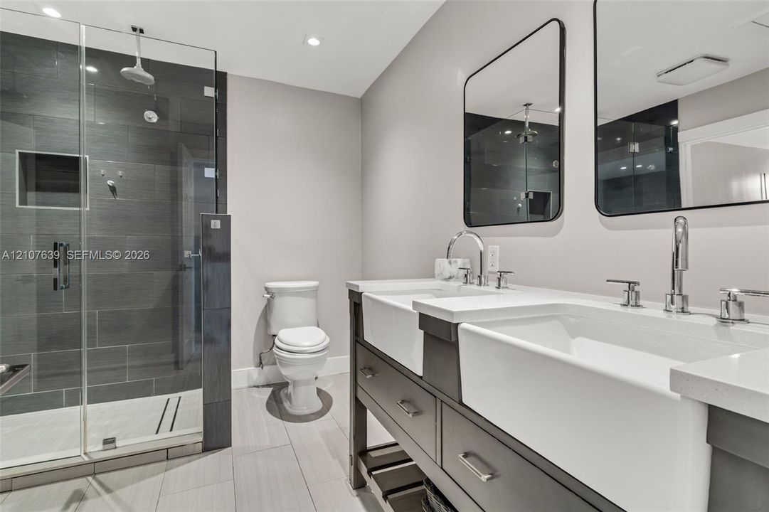 Double vanity featuring farmhouse-style sinks, quartz countertops, glass-enclosed shower with tiled walls, and dual rectangular wall-mounted mirrors