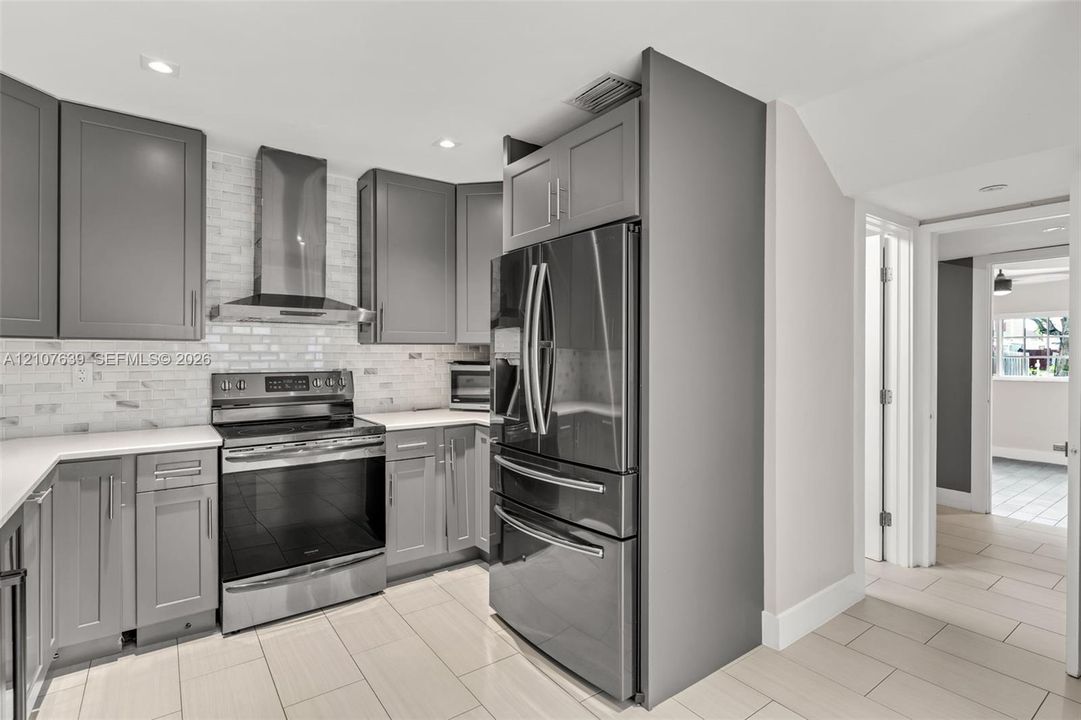 Kitchen featuring grey shaker-style cabinetry, white tile backsplash, stainless steel appliances, and large-format floor tile